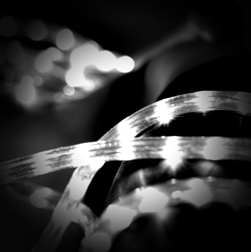 Black and white close-up photograph of illuminated ribbon-like strands, LED light strips, creating a layered, abstract pattern. 
